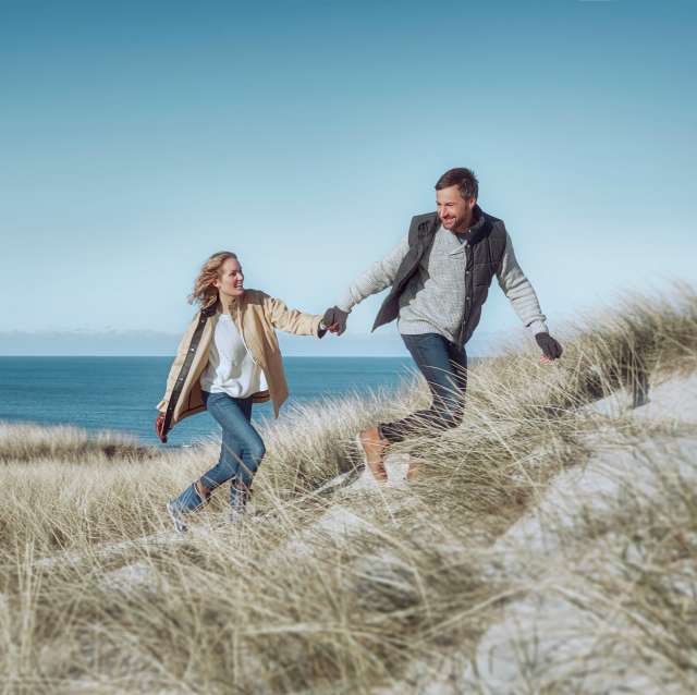 mann-frau-laufen-ueber-duenen-am-meer